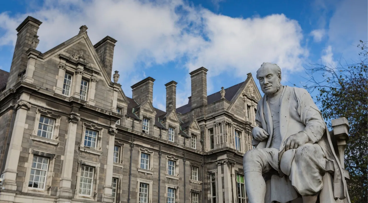 Scholar statue in Trinity College courtyard with the historic stone buildings of the College behind